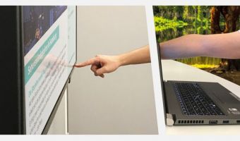 Person interagiert mit einem interaktiven Digital Signage Bildschirm, während sie einen Laptop benutzt.