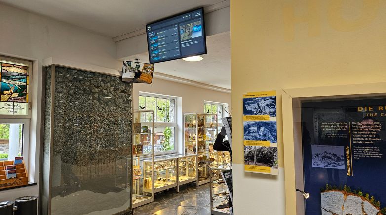 Das Bild zeigt eine digitale Infotafel der Tropfsteinhöhlen Rübeland mit Führungen, Uhrzeiten, Verfügbarkeit und einem Infotext.